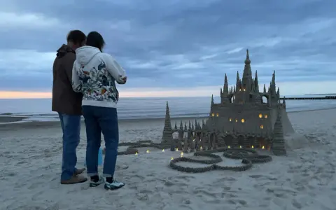 Para podziwia imponujące zamki z piasku na plaży, w okolicach Kołobrzegu. Wieczorne światła dodają magii.