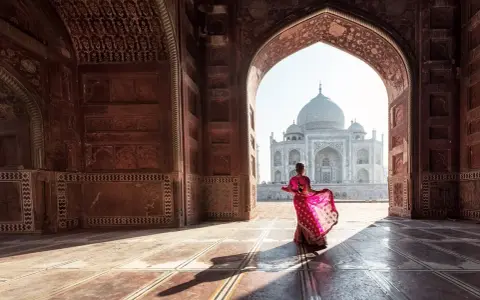 Una mujer con un sari rosa vibrante baila bajo un arco, revelando el Taj Mahal. Descubre curiosidades del Taj Mahal.