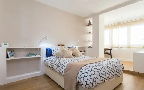 Habitación moderna con cama, estanterías y una apertura que permite tirar tabique para unir dos habitaciones.