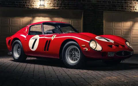 Roter Ferrari 250 GTO, das seltenste Auto der Welt, mit der Startnummer 7, steht vor einer Garage.