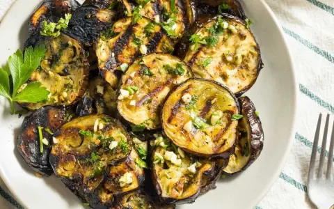 Rodajas de berenjenas a la plancha, doradas y tiernas, con ajo picado y perejil fresco. Un plato sencillo y delicioso.