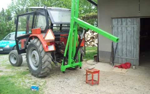 Czerwony traktor z zamontowanym zielonym ładowaczem TUZ przed budynkiem gospodarczym.