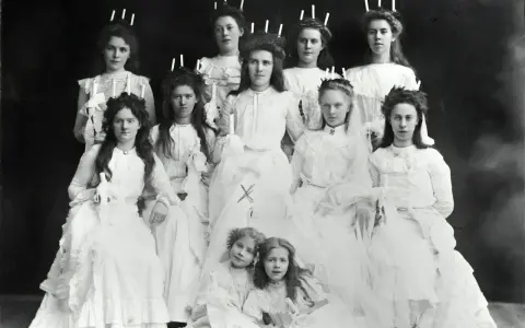 En grupp flickor i vita klänningar, några med ljus i håret, visar hur Lucia såg ut förr.