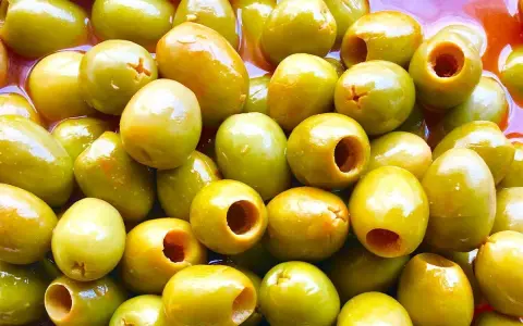 Un primer plano de muchas aceitunas verdes, algunas deshuesadas, listas para ser parte de las clases de aceitunas para comer.