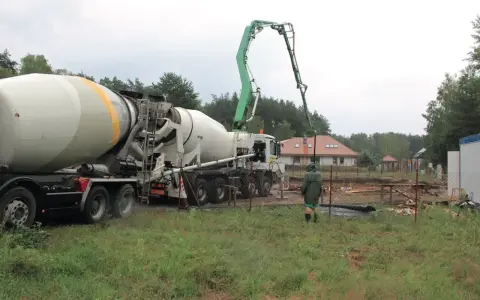 Betoniarka z wysięgnikiem pompuje beton. Pracownik w zielonej kurtce obserwuje. To ważny etap budowy, a czyszczenie betoniarki po pracy, jak usunąć zaschnięty beton z betoniarki, jest kluczowe.