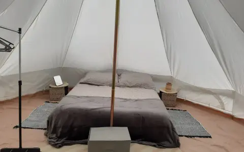 Komfortowy glamping nad morzem: łóżko z pościelą, stoliki nocne, wieszak i namiot.