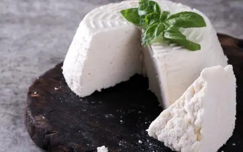 Świeża ricotta z bazylią na ciemnej desce.