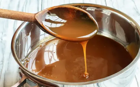 Caramelo líquido cayendo de una cuchara de madera a una olla, perfecto para tu flan al estilo Eva Arguiñano.