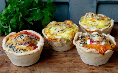 Vier köstliche Mini-Quiches mit verschiedenen Füllungen, perfekt für ein schnelles mini quiche rezept. Mit Petersilie garniert.