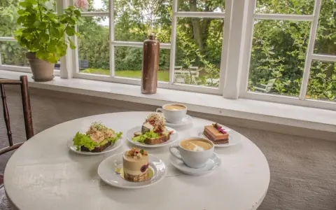 Fika på ett mysigt cafe i Skåne med smörgåsar, tårtor och kaffe.
