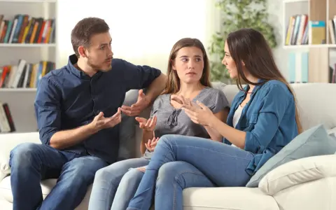 Tres personas sentadas en un sofá blanco discuten animadamente, gesticulando con las manos, en un intento por resolver conflictos.