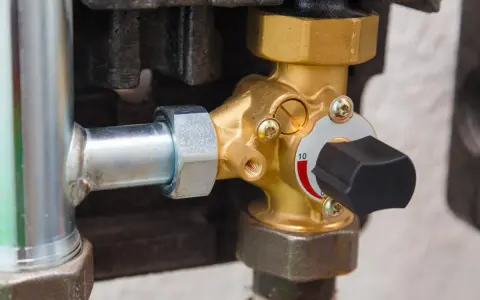 Dettaglio di una valvola pressione acqua caldaia in ottone con manopola nera e indicatore numerico.