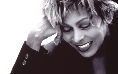 Tina Turner lächelt mit geschlossenen Augen, die Hand am Kopf. Ein ikonisches Bild der Musiklegende.