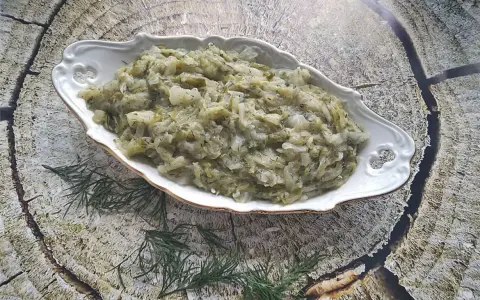 Pyszna kapusta zasmażana z koperkiem, podana w ozdobnej misie na tle drewnianej tekstury.