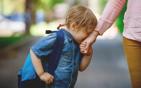 Niña con mochila azul llora y se aferra a la mano de su madre. Parece que mi hija no quiere ir al colegio.