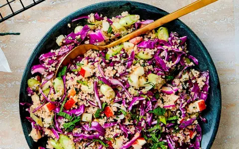 En färgglad couscous sallad med rödkål, äpple och mynta. En gyllene sked vilar i den fräscha rätten.
