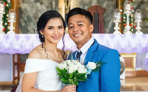 Novios sonriendo, ella con vestido blanco y él con traje azul. Un ramo de rosas blancas. Agradecimiento a los novios por la boda.
