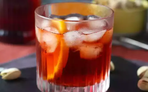 Szklanka z czerwonym drinkiem, lodem i plasterkiem pomarańczy.
