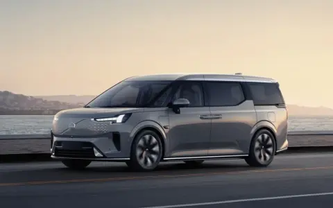 Szary Volvo EM90 jedzie wzdłuż wybrzeża o zachodzie słońca.