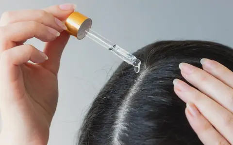 Eine Hand trägt mit Pipette ein Serum auf die Kopfhaut auf, um trockene Schuppen loswerden.