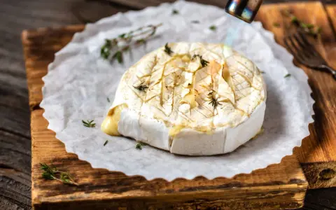 Topiony camembert w ciąży, zapiekany palnikiem z ziołami, na desce.