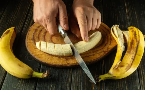Dłonie kroją banana na desce. To świetny pomysł, co jeść na skurcze nóg, bo banany są bogate w potas.