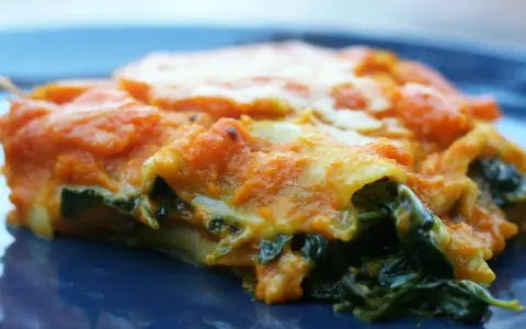 Pyszne lasagne ze szpinakiem, z pomarańczowym sosem i ciągnącym się serem, na granatowym talerzu.