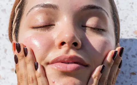 A woman's face, with eyes closed and skin glowing, touches her cheek. It makes you wonder, can your skin type change with the seasons?