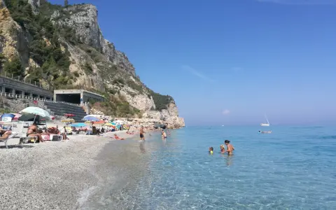 Varigotti spiaggia più bella: gente rilassata sotto gli ombrelloni, mare cristallino e scogliere imponenti.