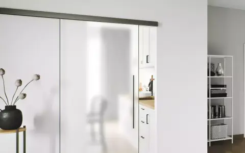 Puerta corredera de cristal esmerilado con tirador negro. Una guía superior negra y un riel inferior negro son clave para como poner una puerta así.