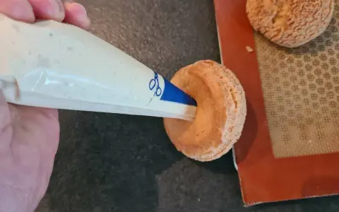 Garnissage d'une pâte à choux profiterole avec une crème onctueuse à l'aide d'une poche à douille.
