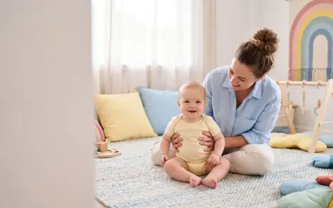 Uśmiechnięta mama wspiera dziecko, które jeszcze nie siedzi. Wspólna zabawa i ćwiczenia to klucz do rozwoju.