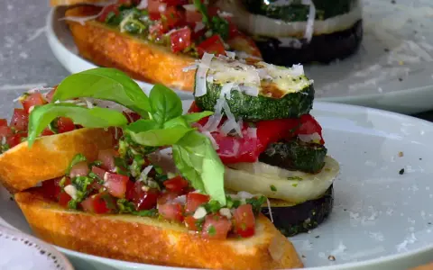 Vegane Grillrezepte: Bruschetta mit Tomaten und gegrilltem Gemüse-Turm, garniert mit Basilikum und Parmesan.