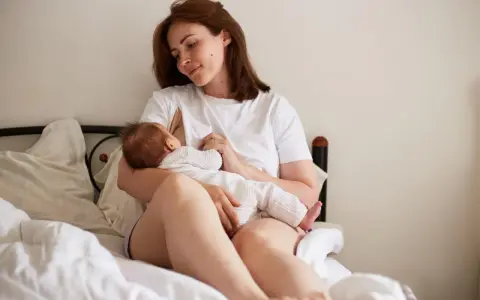 Matka karmi piersią dziecko na łóżku. To piękny obrazek z okresu 12-miesięczny okres ochronny po urlopie macierzyńskim.