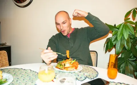Mann feiert sein **Essen nach Marathon** mit einem kräftigen Bizeps-Zeigen und einem Bissen vom Teller.
