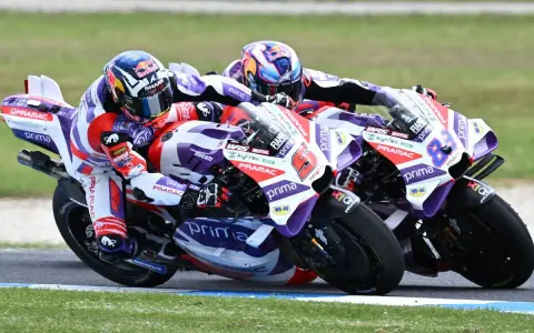 Dos pilotos de MotoGP compiten en una carrera emocionante. El piloto número 6, con casco rojo y blanco, lidera, seguido de cerca por el número 88.