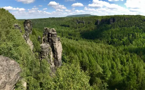 Felsformationen im Bielatal, ideal zum Wandern. Ein Wanderer genießt die Aussicht auf den dichten grünen Wald unter blauem Himmel.