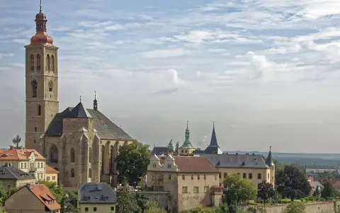Majestatyczna katedra i zabytkowe budynki w Kutnej Horze pod błękitnym, chmurnym niebem.