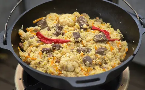 Herzhaftes Plov-Rezept im Kessel: Reis, Fleisch, Karotten, Knoblauch und scharfe Chilis. Ein Festmahl!