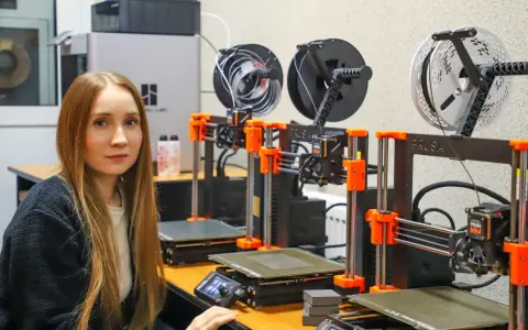 Kobieta w laboratorium obok rzędu drukarek 3D, które są kluczowe dla historii drukarki 3d.