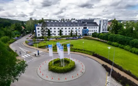 Nowoczesny budynek WSB Gdańsk otoczony zielenią. Na rondzie powiewają białe flagi z logo uczelni.