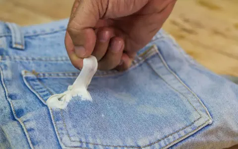 Mano quitando chicle pegado en bolsillo de jeans. Aprende como quitar chicle de la ropa fácilmente.