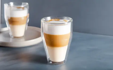 Dwa latte macchiato w szklankach z podwójnymi ściankami, z wyraźnie widocznymi warstwami mleka i kawy.