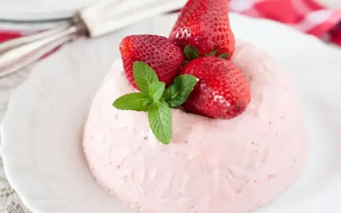 Deliziosa bavarese alle fragole, guarnita con fragole fresche e menta, su un piatto bianco.
