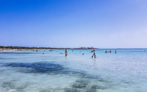 Słoneczny dzień na plaży Es Trenc. Ludzie kąpią się w krystalicznie czystej wodzie, ciesząc się wakacjami.