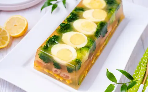 Eleganckie jajka w galarecie z brokułami i kukurydzą, ozdobione plasterkami cytryny.