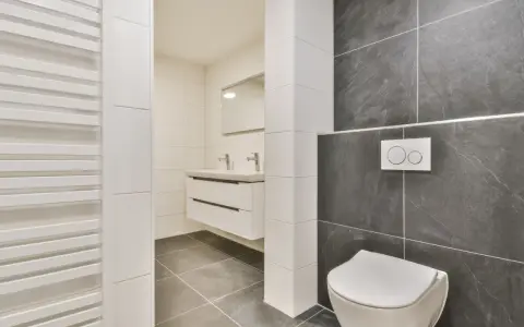 Salle de bain moderne avec wc suspendu, carrelage gris anthracite et blanc, lavabo suspendu et radiateur blanc.