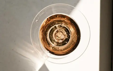 Szklanka z różowym, musującym winem, które wygląda jak tanie wino, ale jest podane w elegancki sposób. Bąbelki unoszą się ku górze.