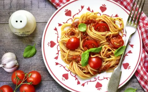 Makaron spaghetti z sosem pomidorowym, pomidorkami koktajlowymi i bazylią na talerzu.