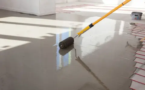 Wałek do wylewki rozprowadza świeżą masę po podłodze z ogrzewaniem podłogowym.